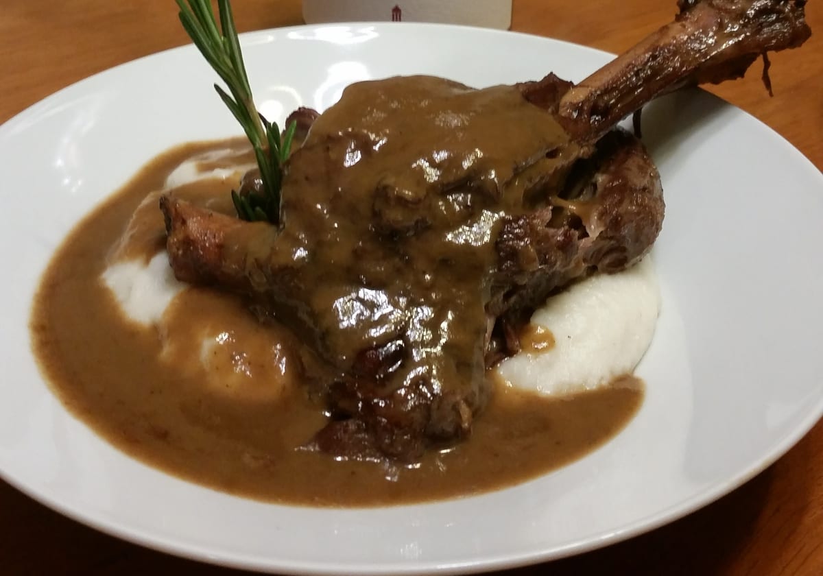 A braised lamb shank under pan gravy, on mashed potato, finished with rosemary