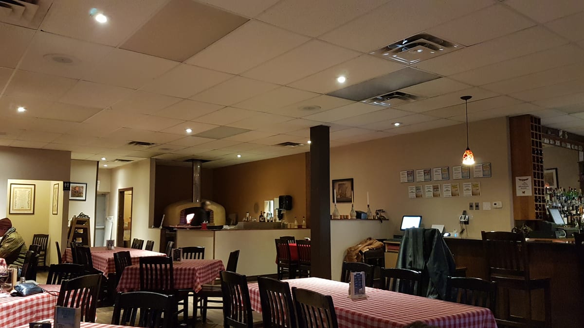 The Amici dining room, red checked tablecloths, the wood-burning oven lit at the back and framed awards along the wall