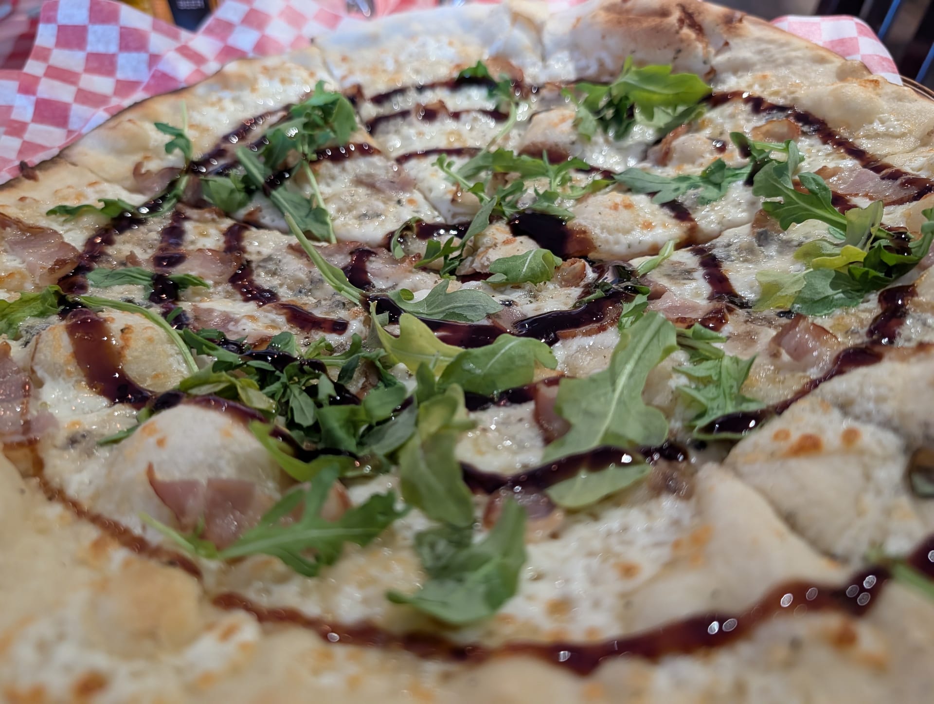 A thin-crust pizza at Amici, with bocconcini, cured meat, fresh arugula and balsamic glaze, on a red checked liner