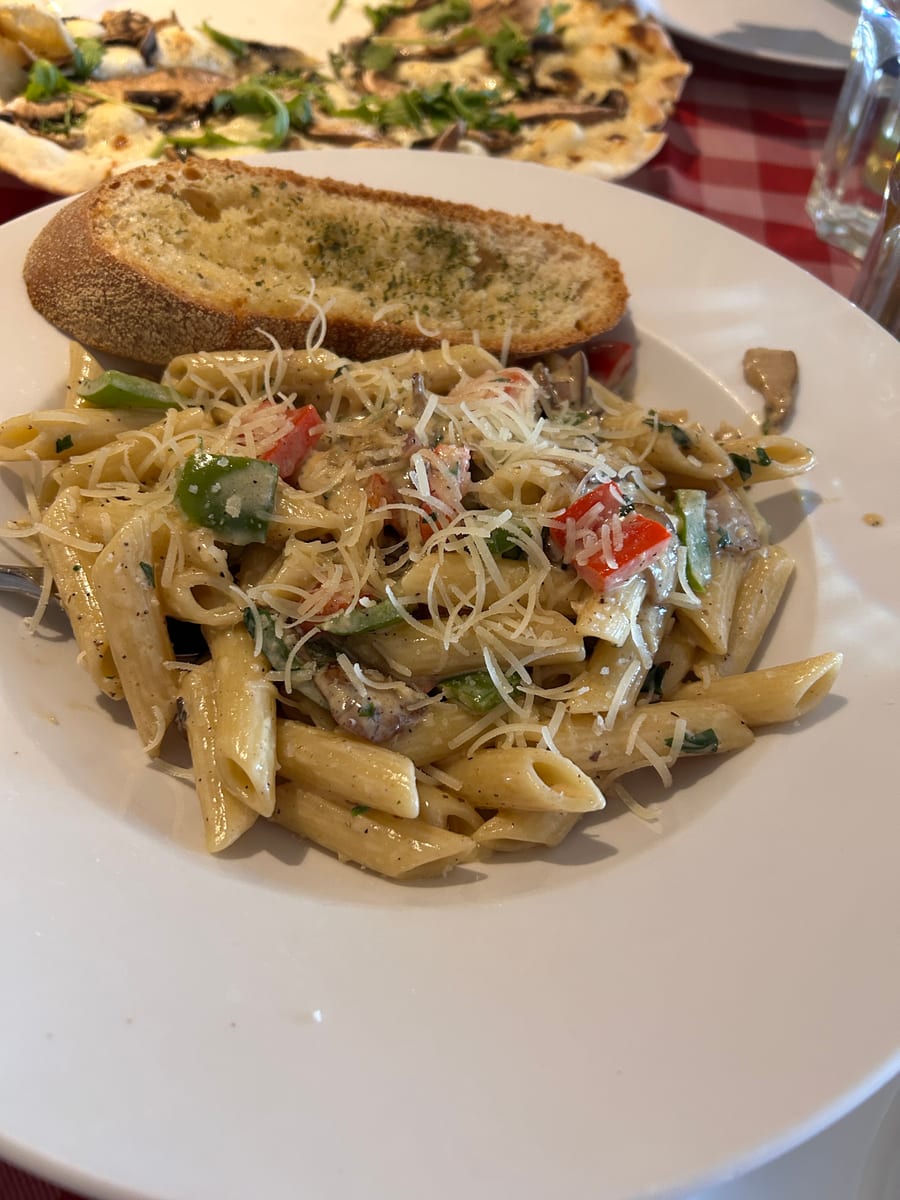 Penne with peppers, mushrooms and shaved Parmesan, garlic bread tucked behind it