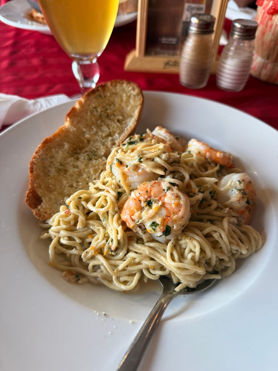 Shrimp tossed through long pasta in a pale sauce, with a slice of garlic bread on the plate