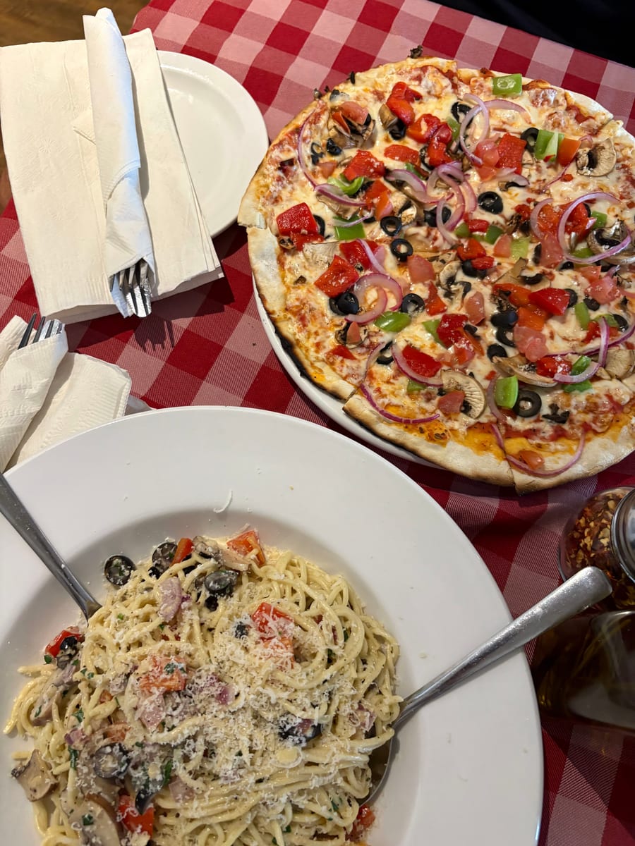 A pizza and a bowl of pasta on a red checked tablecloth at Amici, cutlery wrapped in napkins beside them