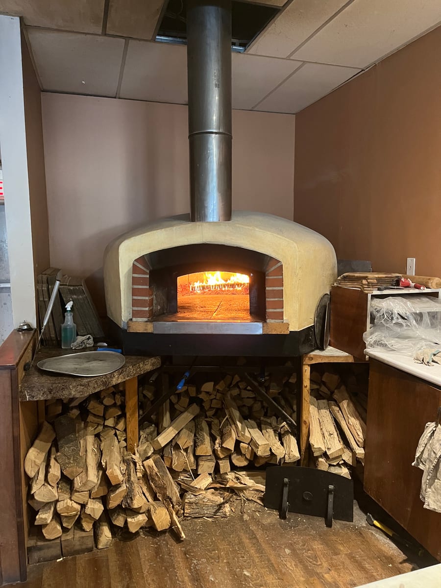 The wood-burning oven at Amici, lit, with split hardwood stacked underneath it